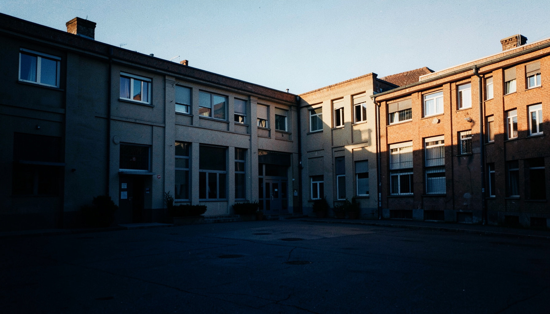 Wide documentary photograph of a calm municipal building courtyard at golden hour, with warm amber sunlight and deep navy shadows